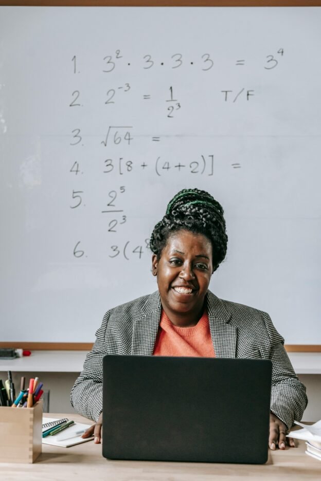 Cheerful African American female using netbook and smiling while looking at camera in classroom with whiteboard