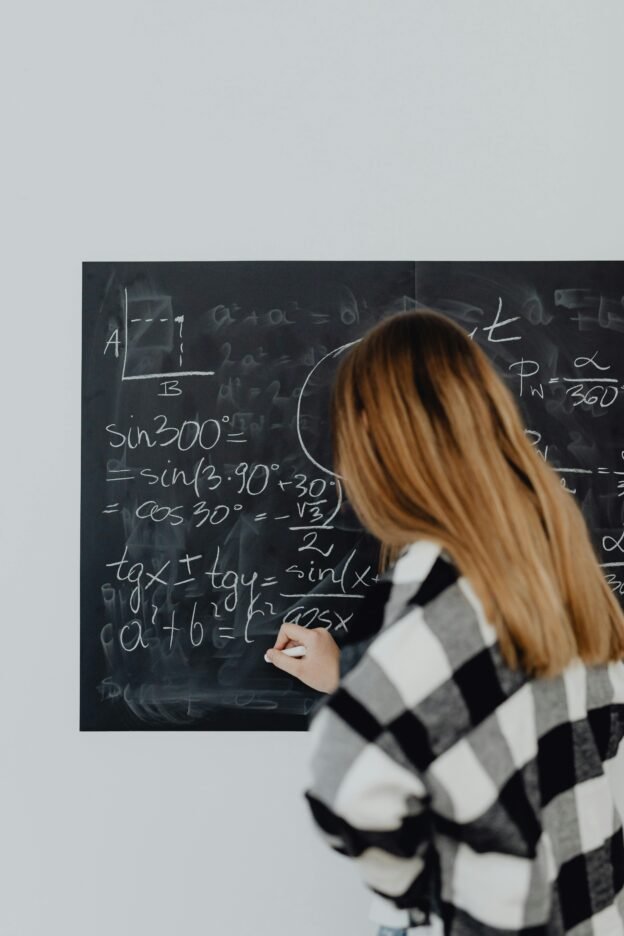 Teenage girl solving math equations on a chalkboard in classroom.
